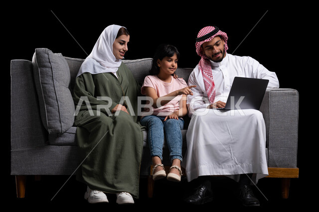 إجراء مكالمات الفيديو والبثوث المباشره من خلال مواقع التواصل الاجتماعي، بورتريه لعائله عربيه خليجيه سعوديه تجلس على الأريكه في غرفه المعيشه أمام الحاسوب المحمول، التفاعل مع العالم الافتراضي عن طريق مشاهدة الأفلام والمسلسلات والتسوق الالكتروني، خلفيه سوداء