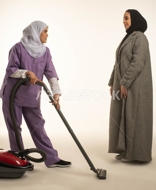توفير خدمات العناية بالمنزل والنظافة والترتيب، اصغاء العاملة المنزليه الى طلبات ربة المنزل، بورتريه لسيدة عربية خليجية سعودية تعطي الارشادات والتوجيهات لخادمة افريقية تقوم باستخدام المكنسة الكهربائية، استقدام العمالة الخارجية المرخصة والمؤهلة، خلفية بيضاء