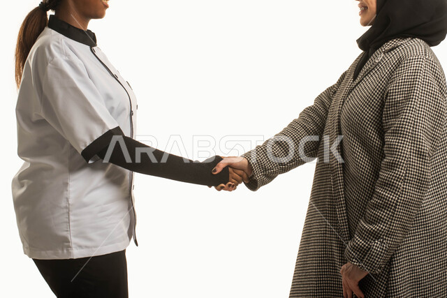 Women's business, professions and jobs, operating cooks licensed and qualified by Saudi companies and offices, a close-up portrait of a veiled Saudi Arab woman shaking hands with an African cook dressed as a chef, receiving and welcoming trained domestic 