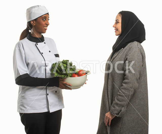  تدريب العاملات المنزليه وشرح طريقة الطبخ العربي السعودي التقليدي، بورتريه مقرب لسيدة عربية خليجية سعودية محجبة تقوم بإعطاء طلبات وتعليمات الطبخ لطباخة افريقية، استقدام الطباخات المرخصة والمؤهلة من الشركات والمكاتب السعوديه، مهن ووظائف نسائية، خلفية بيضاء