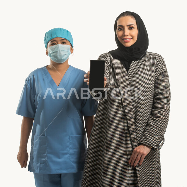 تلبية مطالب الرعاية الصحية عن بعد باستخدام التكنولوجيا، شركات التمريض والطبابة المنزلية في السعوديه، بورتريه لسيدة عربية خليجية سعودية مبتسمة تحمل جوال بشاشة سوداء وممرضة افريقية ترتدي الكمامة و زي التمريض، استقدام العماله المرخصه والمؤهله، خلفية بيضاء
