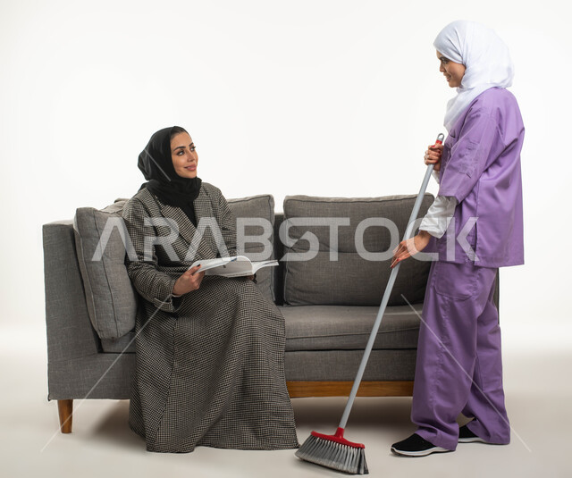 Supervision and guidance of the housekeeper on the cleaning service, a maid cleaning with a hand broom, routine household chores and tasks, a portrait of a veiled Saudi Arabian Gulf woman sitting on the sofa reading books and hiring a foreign maid inside 