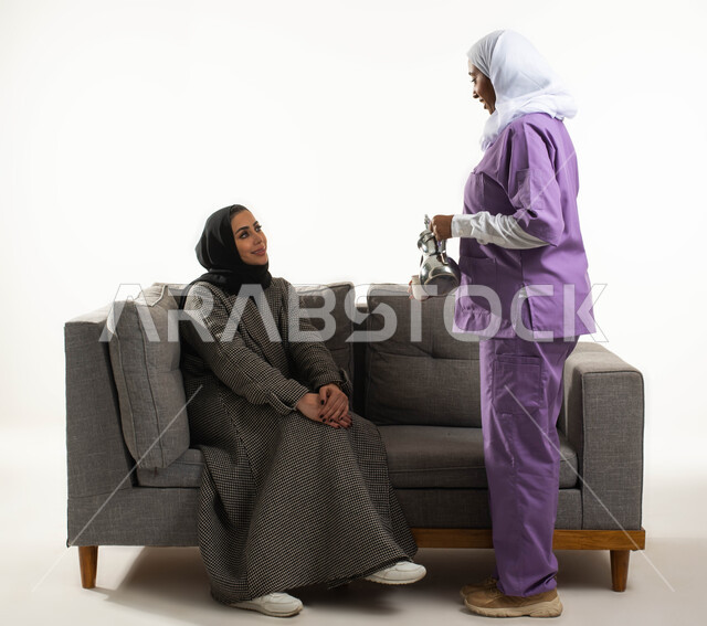 حسن الضيافة والاستقبال، الإحسان في التعامل مع الخادمات في البيوت السعودية، القيام بالمهام والأعمال المنزلية الروتينية، مدبرة منزل تستعين بخادمة أجنبية، بورتريه من الجانب لخادمة فلبينية تقوم بصب القهوة لسيدة عربية خليجية سعودية محجبة، خلفية بيضاء.