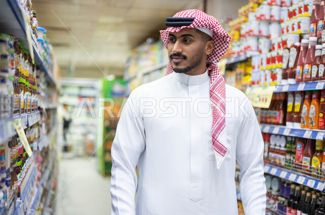 Having different purchase and consumption options in the mall, displaying local and national products in the market, ease and comfort in shopping, having a good time choosing household supplies, a close-up of a Saudi Arabian Gulf man wearing traditional c