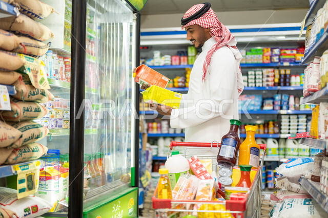 اختيار السلع والمواد الغذائية المختلفة, قراءة محتويات ومكونات العصير, رجل عربي سعودي خليجي يرتدي الثوب التقليدي يقوم بانتقاء العصائر  الطازجه الغير صناعيه, الحيرة في الحصول المنتج الأفضل,متعة الشراء والتسوق في احدى المتاجر والبقالات السعوديه