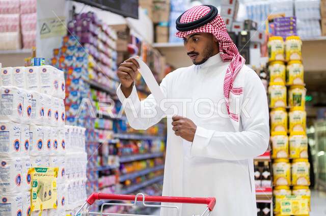 إيماءات تدل على الدهشة والذهول والصدمة, رجل عربي سعودي خليجي يرتدي الثوب التقليدي يقوم بقراءة قائمة المشتريات, غلاء أسعار المستلزمات المنزلية, شراء اللوازم والاحتياجات الغذائية, أهمية الاستفادة من العروض والتخفيضات  على المنتجات