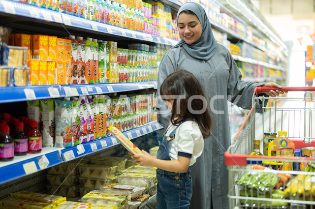 Spending a good time in the malls in the Kingdom of Saudi Arabia, the joy of shopping with children, a smiling Gulf Arab woman wearing an abaya and hijab shopping in the supermarket accompanied by her daughter, a Saudi girl choosing her favorite product, 