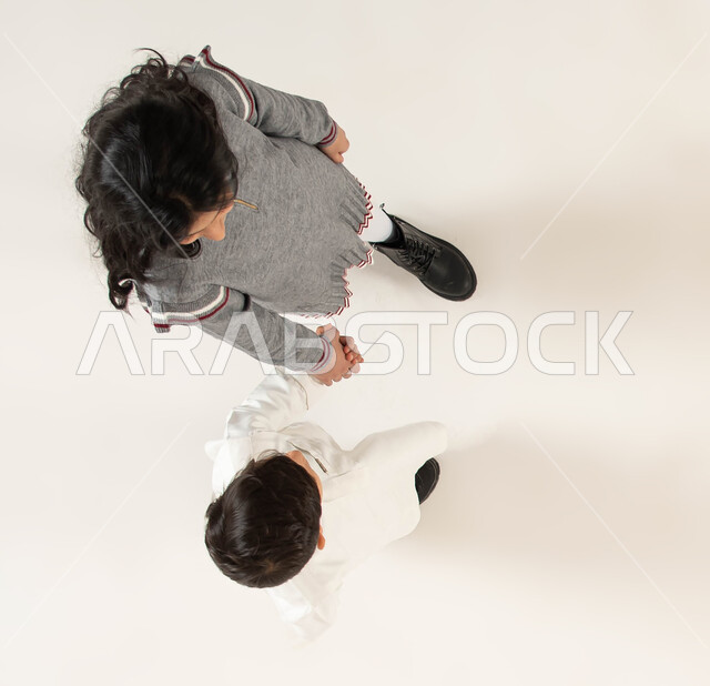 ايماءات السير والذهاب لقضاء أوقات ممتعة مع الأخوات, تعزيز وتقوية العلاقة الإيجابية بين الأخوة, بورتريه علوي عامودي لأخويين عربيين سعوديين خليجيين يمسكان بيد بعضهما, مفهوم الألفة والمحبة والترابط الأخوي, خلفية بيضاء