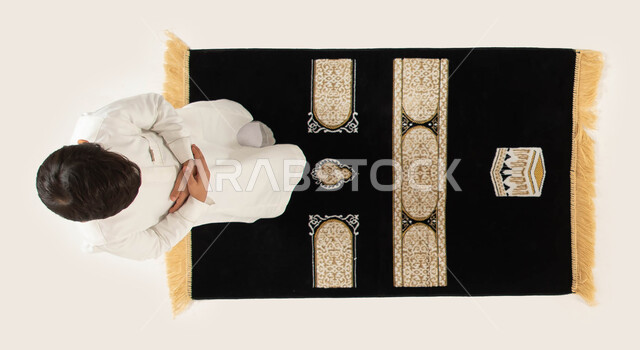 إسلاميات وعبادة, التقرب من الله تعالى بأداء الفرائض والتزام أوامره, بورتريه علوي عامودي لولد عربي خليجي سعودي يرتدي الثوب التقليدي ويصلي لله تعالى, أهمية تعليم الأطفال الالتزام بالصلاة على وقتها, مفهوم أركان الإسلام, خلفية بيضاء