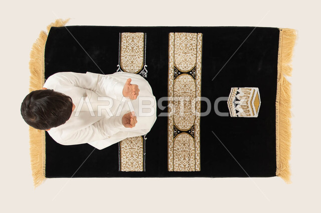 الجلوس على سجادة الصلاة والقيام بالأذكار والأدعية اليومية, الدعاء والتقرب من الله تعالى, بورتريه علوي عامودي لطفل عربي خليجي سعودي يرتدي الثوب التقليدي يقوم بالدعاء الى الله, مفهوم أركان الإسلام, إسلاميات وعبادة, خلفية بيضاء