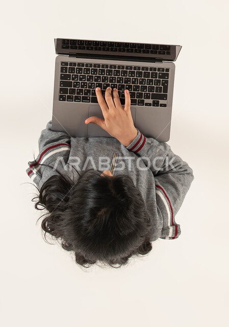 اللعب و الترفيه وقضاء اوقات مسلية باستخدام التكنولوجيا الحديثة، دورات اونلاين تعلمية ثقافية وانشطة ترفيهية الكترونية للاطفال، التعلم وتلقي دروس الاونلاين عن بعد، بورتريه علوي عامودي لفتاة عربية خليجية سعودية تستخدم جهاز الحاسوب المحمول، خلفيه بيضاء.