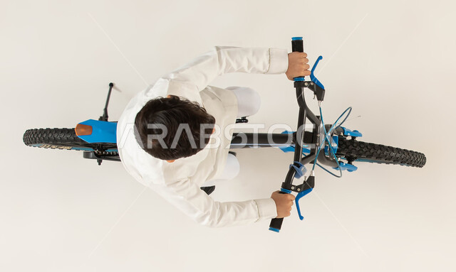 Physical activity to maintain physical fitness, participating in bicycle racing, practicing the hobby of riding bicycles, vertical portrait of a Saudi Arabian Gulf boy riding a bicycle, spending time learning fun and entertaining activities for children, 