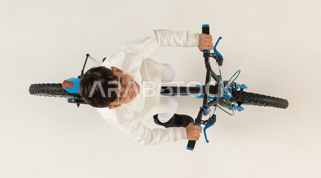 Participating in a bicycle race, practicing the hobby of riding bicycles, a vertical portrait of a smiling Saudi Arab Gulf boy riding a bicycle looking at the camera, spending time learning fun and entertaining activities for children, physical activity t