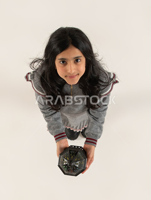 التجهيزات لاستقبال شهر رمضان المبارك، بورتريه علوي عامودي لبنت عربيه خليجيه سعوديه مبتسمة تحمل بيدها الفانوس الرمضاني تنظر الى الكاميرا، المناسبات الدينيه والأعياد الإسلامية، التزيين والتحضير للأجواء الروحانيه الرمضانيه، اسلاميات و عبادة، خلفيه بيضاء.