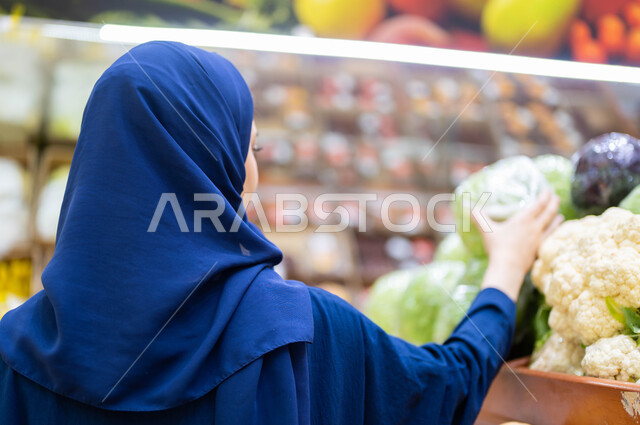 محاصيل زراعية ومنتجات وتموينات مستوردة ومحلية في البقالة السعودية, صورة مقربة من الخلف لإمرأة عربية سعودية خليجية محجبة ترتدي العباءة تقوم باختيار الأفضل والأجود من الملفوف الطازج, التسوق وشراء اللوازم الغذائية الصحية من مراكز التسوق