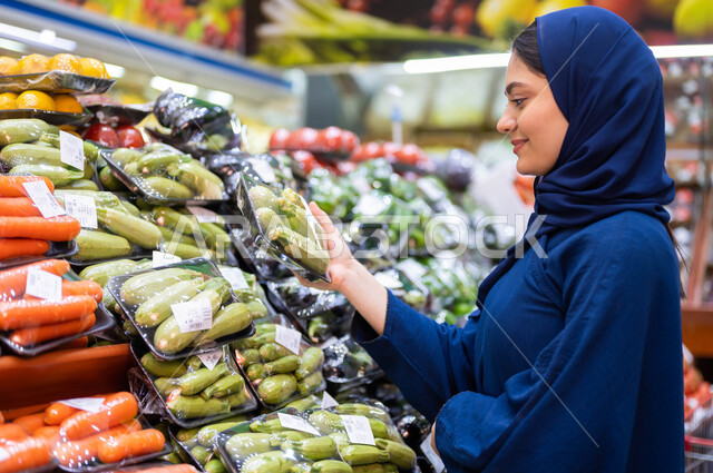 مستلزمات المستهلك السعودي, انتقاء أفضل وأجود الخضراوات الموجودة في السوبرماركت, صورة مقربة لشابة عربية سعودية خليجية في إحدى أقسام الخضراوات تقوم بشراء الكوسا الطازجة, المنتجات والمحاصيل الزراعية المحلية وتموينات مستوردة في المحلات التجارية