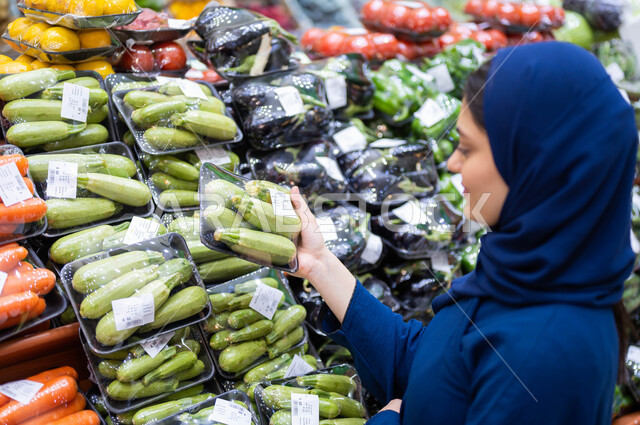 انتقاء أفضل وأجود الخضراوات الموجودة في السوبرماركت, صورة مقربة لشابة عربية سعودية خليجية في إحدى أقسام الخضراوات تقوم بشراء الكوسا الطازجة, المنتجات والمحاصيل الزراعية المحلية وتموينات مستوردة في المحلات التجارية, مستلزمات المستهلك السعودي