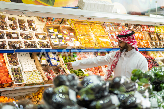 إختيار أجود أنواع الفاكهة والخضراوات الطازجه في السوبرماركت، رجل عربي خليجي سعودي يرتدي الزي التقليدي يقوم بالإشاره إلى أحد أنواع المواد الغذائيه النباتيه في قسم الفواكه والخضار الموسميه، شراء المنتجات المحلية الوطنية, محاصيل زراعية سعودية. 