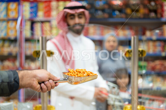 قضاء الوقت في التسوق برفقة العائلة، أسرة عربية خليجية سعودية تقوم بشراء التسالي والمقرمشات الطازجه من السوبرماركت، التعاون ومشاركة العائلة في إختيار أنواع مختلفة من المكسرات من الماركت، استغلال العروض في توفير الاحتياجات المنزلية.
