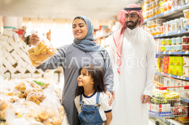 Spouses’ cooperation in purchasing food supplies, the concept of shopping and purchasing household supplies with the family, a Saudi Arabian Gulf family choosing bread from the bakery section in the supermarket, benefiting from offers, sales and discounts on food commodities.
