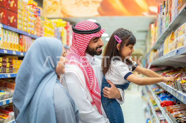 التمتع بالتخفيضات والعروض والخصومات على المنتجات، التعاون في شراء السلع والمواد الغذائيه المختلفة في السوبرماركت، زوجان عربيان خليجيان سعوديان يقومان بقضاء أوقات ممتعة بالتسوق واختيار اللوازم المنزليه برفقه ابنتهم، مساعدة وتعليم الأبناء الشراء من الماركت.