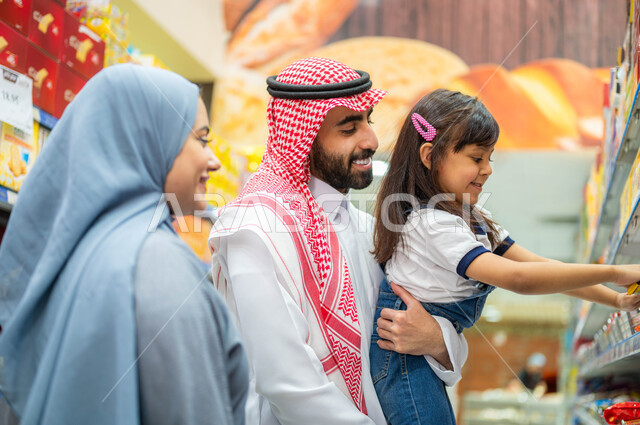 التعاون في شراء السلع والمواد الغذائيه المختلفة في السوبرماركت، زوجان عربيان خليجيان سعوديان يقومان بقضاء أوقات ممتعة بالتسوق واختيار اللوازم المنزليه برفقه ابنتهم، التمتع بالتخفيضات والعروض والخصومات على المنتجات، مساعدة وتعليم الأبناء الشراء من الماركت.