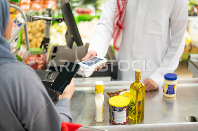 استغلال أيام التخفيضات والعروض والحسومات، قضاء أوقات ممتعه في شراء المستلزمات والمواد الغذائيه من السوبرماركت، سيدة عربية خليجية سعودية تقوم بالمحاسبه عبر الهاتف عند الكاشير، الدفع الالكتروني عن طريق الجوال، منتجات غذائيه محليه وطنيه.