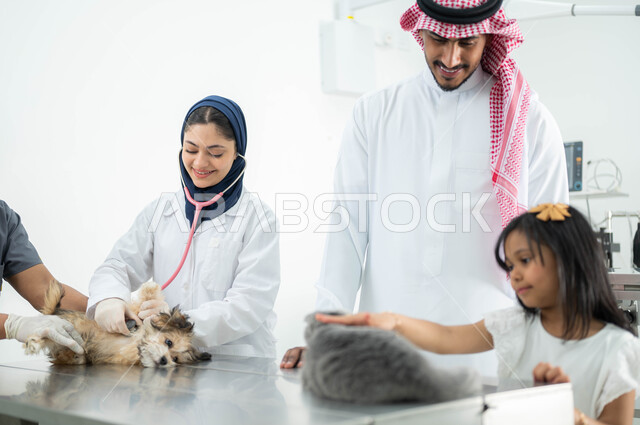 مفهوم الاهتمام والعناية بالحيوانات المنزلية، ضرورة الفحص الطبي الدوري للحيوانات الأليفة, طبيبة بيطرية محجبة تقوم بفحص ومعالجة كلب صغير، رجل سعودي عربي خليجي يرتدي الثوب التقليدي والشماغ يقوم بزيارة المراكز والعيادات البيطرية برفقة ابنته