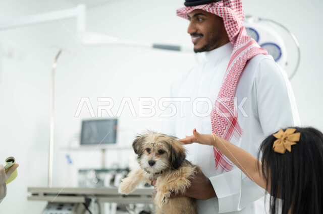 الزيارة الدائمة للعيادات البيطرية والاعتناء بالحيوانات المنزلية, المرح واللعب مع حيوان الكلب الأليف, أب سعودي عربي خليجي يرتدي الزي التقليدي يقوم بزيارة مراكز الطبية الخاصة  بالحيوانات برفقة ابنته,  مفهوم الرفق بالحيوان والعطف عليه