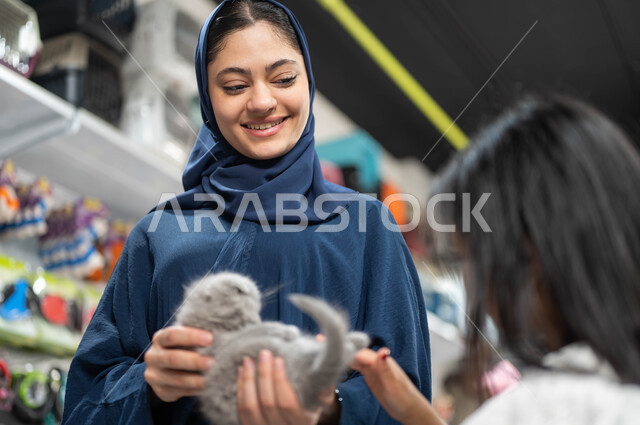 التسوق للمنتجات اللازمة الخاصة بالحيوان الاليف، صورة مقربة لفتاة عربية خليجية سعودية تقوم باللعب مع القطة الرمادية المدللة برفقة والدتها، مفهوم الرفق بالحيوانات والعطف عليهم والاهتمام بهم، متاجر بيع وشراء مستلزمات وإكسسوارات القطط والكلاب
