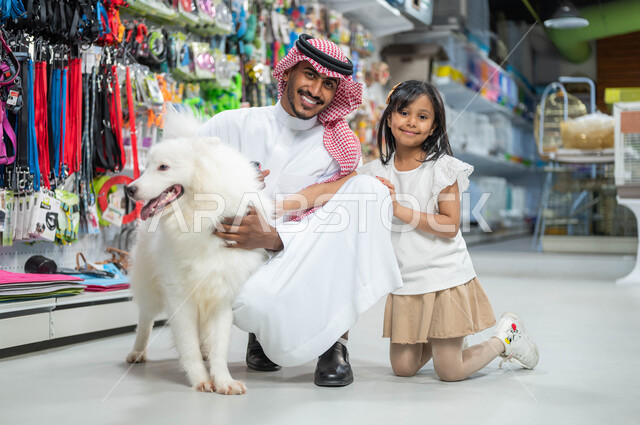 ايماءات السعادة والمرح واللعب مع الكلب الأبيض الوفي، رجل عربي خليجي سعودي مبتسم يرتدي الزي السعودي التقليدي ينظر إلى الكاميرا يجلس برفقة ابنته الصغيرة، متاجر بيع وشراء حاجات مستلزمات الحيوانات الأليفة، مفهوم الرفق بالحيوان الودود المخلص
