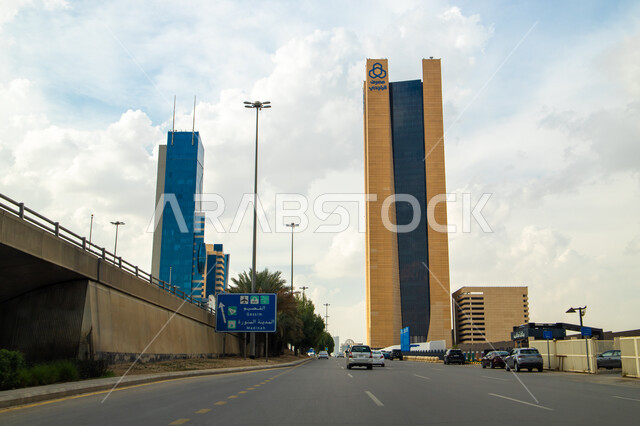 منظر السحب البيضاء الكثيفة في سماء المملكة العربية السعودية في وضح النهار، حركة سير السيارات في طريق الملك فهد في الرياض، أماكن ومعالم سياحية مشهورة في مدينة الرياض، الفن الهندسي المعماري في الأبراج وناطحات السحاب، تصاميم هندسية متطورة وحديثة