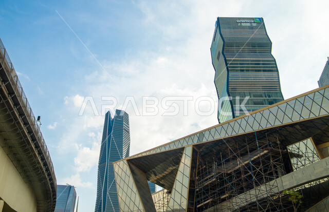 صورة من الزاوية لأبراج مركز الملك عبدالله المالي (كافد) في الرياض بالمملكة العربية السعودية، الاستمرار في تطوير وتحديث التصاميم الهندسية  المتميزة للمباني، أماكن ومعالم سياحية مشهورة بالرياض، منظر السحب الكثيفة في السماء في وضح النهار