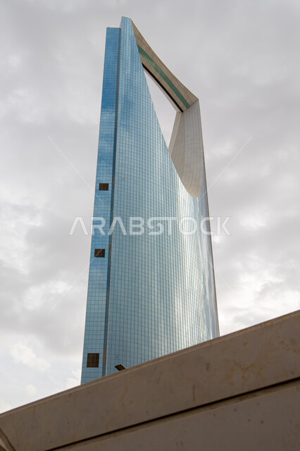 منظر السحب البيضاء الكثيفة في السماء، التصميم المتطور والحديث للأبراج وناطحات السحاب، صورة من الجانب لبرج المملكة في مدينة الرياض، معالم وأماكن سياحية مشهورة في المملكة العربية السعودية، جذب السياح الأجانب إلى داخل السعوديه