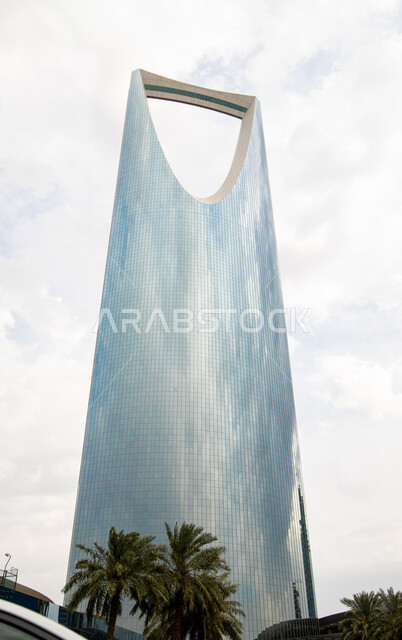 أشجار النخيل الخضراء والسحب البيضاء الكثيفة في السماء، التصميم المتطور والحديث للأبراج وناطحات السحاب، صورة مقربة لبرج المملكة في مدينة الرياض، معالم وأماكن سياحية مشهورة في المملكة العربية السعودية، جذب السياح الأجانب إلى داخل السعوديه