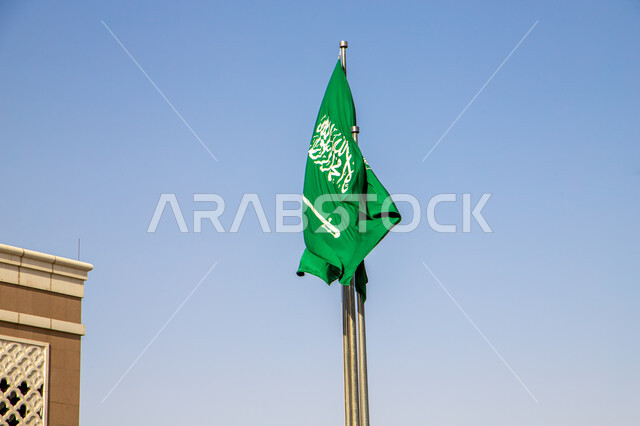 العلم السعودي يرفرف في سماء المملكة العربية السعودية في وضح النهار، الاحتفال بذكرى اليوم الوطني، يوم التأسيس، علم أخضر يحمل عبارة لا اله الا الله، حب الوطن وتقدير الهوية الوطنية، الأعياد الوطنية للمملكه