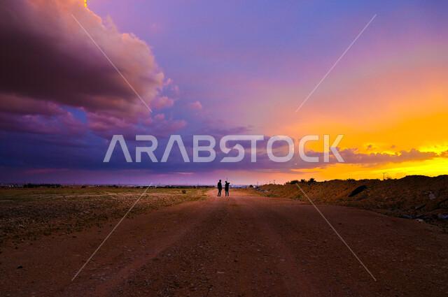 شابان عربيان خليجيان يتجولان وسط الصحراء في المملكة العربية السعودية، الغيوم والسحب في السماء وقت غروب الشمس، المناظر الطبيعية في المناطق الصحراوية