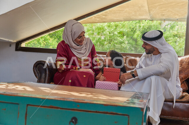 Exchanging conversations and chats with children, a happy family atmosphere full of love, celebrating the advent of the blessed Eid, special sessions with the family, presenting gift boxes to the son, a Saudi Arabian Gulf family sitting in the living room