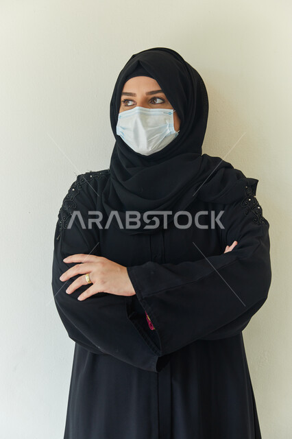 Adhere to the laws and rules of the Ministry of Health to avoid infection with Covid-19, a close-up portrait of a veiled Emirati Arab Gulf woman wearing a black cloak and wearing a muzzle to avoid the spread of the Corona virus, gestures looking at someth