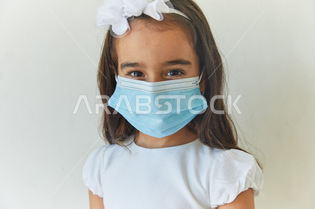 الوعي الصحي وتجنب إنتشار العدوى، مفهوم إتباع الإجراءات الوقائيه لضمان السلامة من فايروس كورونا، بورتريه مقرب لفتاة عربيه خليجيه اماراتية ترتدي فستان أبيض وتضع الكمامة للحمايه من الإصابه بكوفيد-١٩، ايماءات النظر إلى الكاميرا، خلفيه بيضاء.
