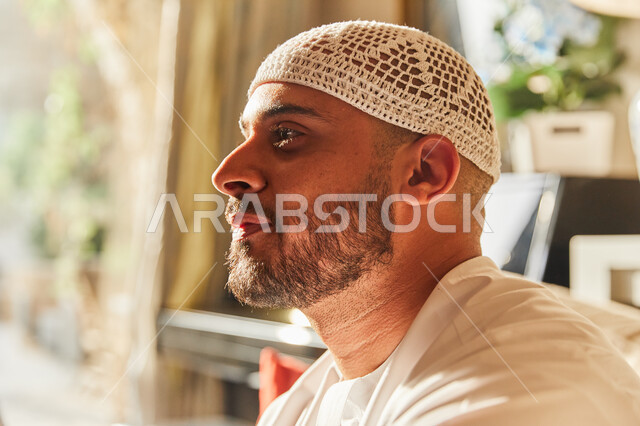  ايماءات الاندماج و شرود الذهن، اتخاذ القرارات و حل المشكلات، صورة جانبية مقربة لرجل عربي خليجي اماراتي يرتدي الكندورة والطاقية الاماراتية البيضاء يقوم بالتفكير والتخطيط للمستقبل، النظر إلى شيء ما.