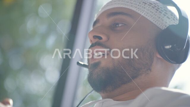 استخدام تقنية الهيدفون، صورة مقربه لرجل عربي اماراتي خليجي يرتدي الطاقية البيضاء والكندورة وسماعه الرأس الصوتية، العمل عن بعد، التسويق الالكتروني من المنزل، تقديم برنامج اذاعي صوتي، الاستمتاع في سماع المقاطع الموسيقيه، التواصل مع الأصدقاء والأقارب