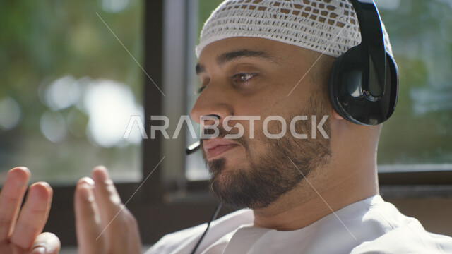 تقديم برنامج اذاعي صوتي، استخدام تقنية الهيدفون، صورة مقربه لرجل عربي اماراتي خليجي يرتدي الطاقية البيضاء والكندورة وسماعه الرأس الصوتية، العمل عن بعد، التسويق الالكتروني من المنزل، إجراء مكالمة فيديو، التواصل مع الأصدقاء والأقارب