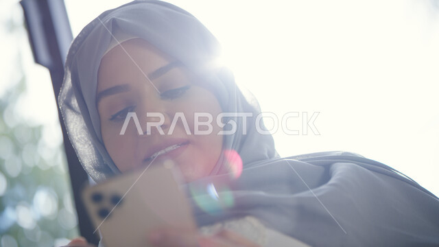 التسوق الالكتروني الذكي والآمن عبر الاونلاين, صورة مقربة لإمرأة عربية خليجية إماراتية محجبة تقوم بالتواصل الاجتماعي عبر الجوال, استخدام التقنيات والتكنولوجيا الحديثة لإنجاز مهام العمل, إدمان استخدام الانترنت والهواتف المحمولة