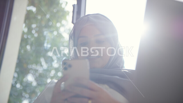 إدمان استخدام الانترنت والهواتف المحمولة، التسوق الالكتروني الذكي والآمن عبر الاونلاين, صورة مقربة لإمرأة عربية خليجية إماراتية محجبة تقوم بالتواصل الاجتماعي عبر الجوال, استخدام التقنيات والتكنولوجيا الحديثة لإنجاز مهام العمل