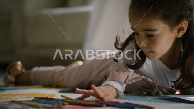 رعاية الأبناء والاهتمام بالهوايات المفيدة, استغلال أوقات الفراغ بالأنشطة الترفيهية الممتعة, صورة مقربة لفتاة عربية خليجية إماراتية تجلس على الأرض وتقوم باستخدام أقلام التلوين, تنمية مهارات الأولاد الذهنية والحركية