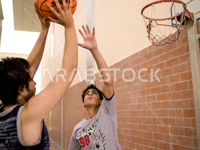 هواية اللعب بكرة السلة، نشاط بدني في الهواء الطلق، اللياقة الجسدية والتسلية والترفيه، صورة مقربة لصبيين عربيين خليجيين سعوديين يرتديان اللباس الرياضي ويلعبان كرة السلة, ممارسة الرياضات في الملاعب العامة، منافسات وتحديات بين الأصدقاء.