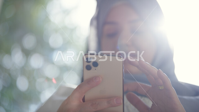 استخدام التقنيات والتكنولوجيا الحديثة لإنجاز مهام العمل, التسوق الالكتروني الذكي والآمن عبر الاونلاين, صورة مقربة لإمرأة عربية خليجية إماراتية محجبة تقوم بالتواصل الاجتماعي عبر الجوال, إدمان استخدام الانترنت والهواتف المحمولة