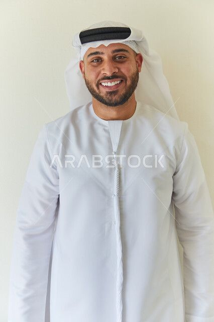 إلتقاط صوره شخصية للوثائق الرسميه، بورتريه مقرب لشاب عربي خليجي إماراتي ينظر إلى الكاميرا بإبتسامة ويرتدي الكندوره والغتره الإماراتيه يقوم بالنظر إلى الكاميرا، الإهتمام بالمظهر الخارجي، خلفيه بيضاء. 
