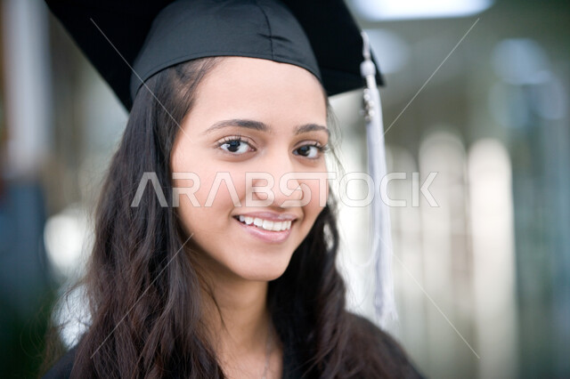 Celebrations of achieving the dream of success from the university, joy and pleasure, and celebration of graduation day with gestures of happiness, a close-up of an Arab Gulf Emirati student wearing graduation uniform and hat holding in her hand a certifi